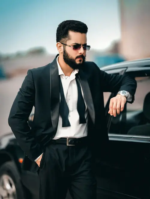 Man in a tuxedo beside a black luxury car