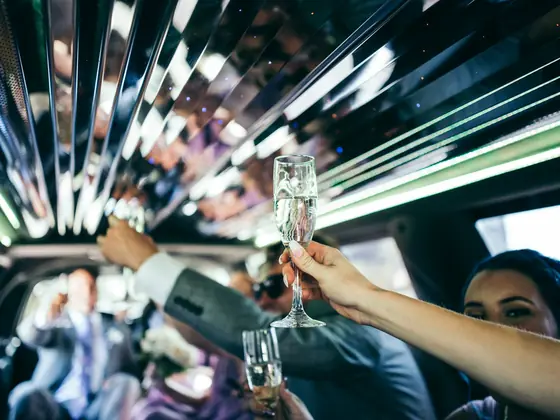 Friends raising champagne glasses under the lights of a party limousine